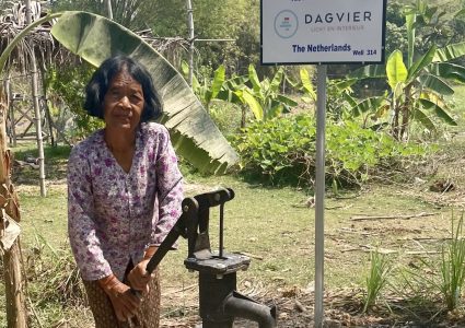 Cambodian woman standing next to waterpump.